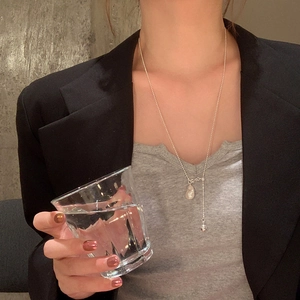 Gros plan d'un collier en Y argenté avec perle baroque et bille en métal sur modèle