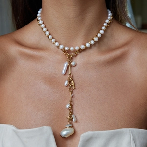 Close-up of gold Y-chain necklace featuring irregular pearls and a small fish charm