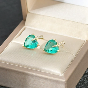 Close-up of golden heart earrings with green gemstone and small diamonds in a gift box