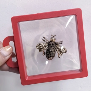 Detailed view of an antique gold bee brooch inside a 3D red suspension display box