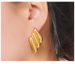 Close-up of model wearing gold wing-shaped earrings with streamlined pleated texture