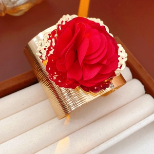 Détail d'un bracelet doré texturé orné d'une grande fleur en tissu rouge sur son support