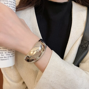 Bracelet jonc ouvert argenté poli porté au poignet avec une veste en tweed et magazine