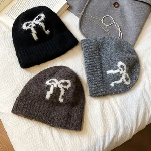 Women's knitted beanies in black, grey, and brown with white bow jacquard pattern