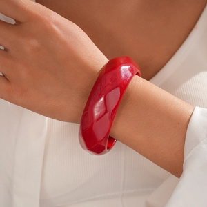 Close-up of a chunky red resin bangle with faceted surface worn by a model in soft light