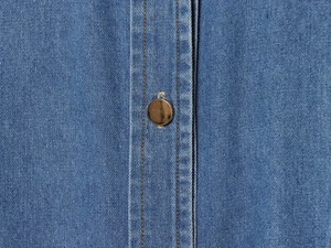 Detail eines blauen Denim-Kleides mit Kupferknopf und klassischen gelben Nähten