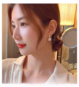 Close-up of elegant pearl drop earrings with gold sparkling zircon hoop on female model