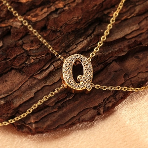 Copper letter Q pendant necklace with clear cubic zirconia on textured bark background