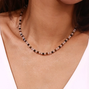 Close-up of beaded necklace with tiger eye stones and gold beads on a model wearing white