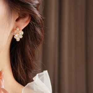 Close-up of elegant gold flower stud earrings with sparkling crystals worn by a model