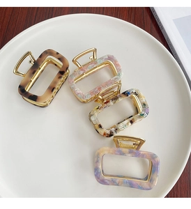 Detail of four acetate hair claws in leopard, floral, and marble patterns on a white tray