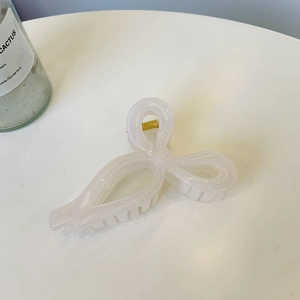 Close-up of a creamy white ribbon hair claw clip with golden metal spring on white table