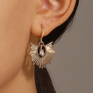 Détail d'une boucle d'oreille soleil dorée avec cristal goutte sur une oreille