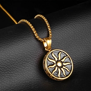 Men's gold sun pendant necklace with black enamel inlay on a dark leather surface