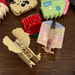 Assorted colorful acetate hair claws in cute dog, house, and fruit shapes on wood