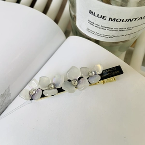 Sweet acetate flower hair clip with rhinestones resting on an open book background