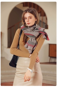 Détail d'une écharpe à carreaux gris avec rayures rouges et franges, portée par un mannequin