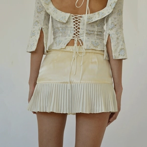 Women's floral crop top with lace-up back and yellow pleated mini skirt with pearl chain