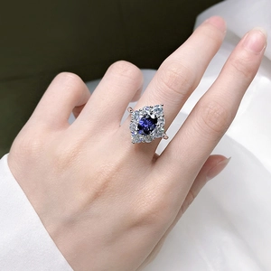 Nahaufnahme eines luxuriösen ovalen blauen Zirkonrings mit Doppel-Halo auf einer Hand
