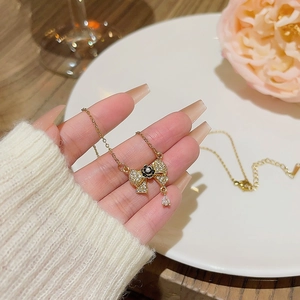 Close-up of golden bow necklace with black flower, sparkling zircons and drop pendant