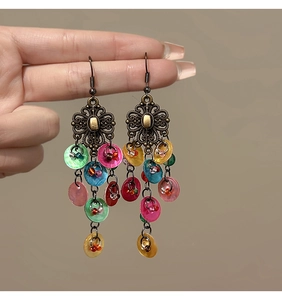 Detail of bohemian drop earrings with colorful shell discs and bronze floral cutouts