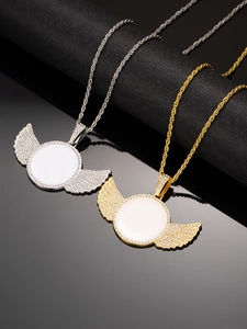 Detail of gold and silver diamond-set wing photo necklaces on black textured surface