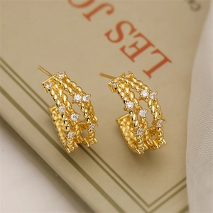Detailed close-up of C-shaped gold hoop earrings with white zircons on vintage book