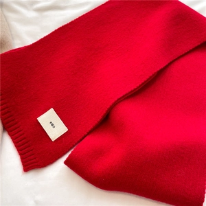 Close-up of a red knit scarf with thick texture and a rectangular emo label detail