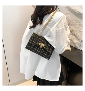Close-up of black plaid tweed shoulder bag featuring golden chain strap and metal lock