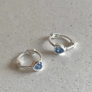Detailed view of silver heart earrings with blue cubic zirconia on stone background