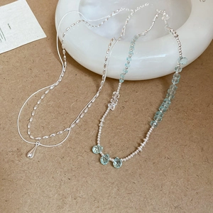 Detail of silver drop pendant layered with blue beaded chain on ceramic plate
