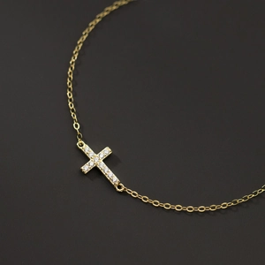 Elegant gold sterling silver cross bracelet with sparkling cubic zirconia on dark background