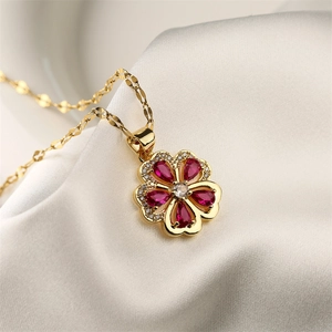 Close-up of gold clover pendant with red and clear gems on white silk background