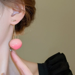 Macro detail of long gold drop earrings featuring a sweet pink gradient resin peach charm
