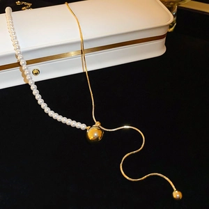 Detail of asymmetric necklace featuring white pearls, golden snake chain, and tassel drop