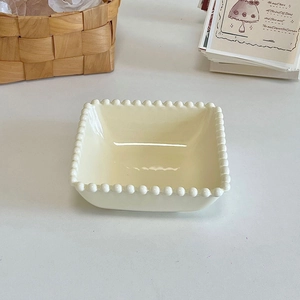 Detail of square cream ceramic dessert plate with beaded edge and glossy texture