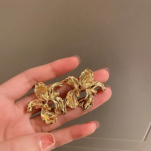 Detail of vintage gold flower earrings with embossed texture held by hand