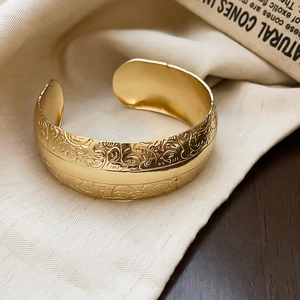 Gros plan d'un bracelet manchette doré avec relief floral vintage sur un tissu en lin