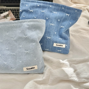 Detailed view of denim makeup bags with embroidered white bows and heart patterns