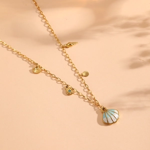 Gold cable chain necklace featuring enamel shells and blue gemstone pendant on peach background