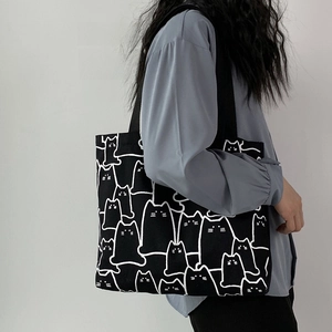 Detail of a large black canvas tote bag featuring playful white cat line art patterns