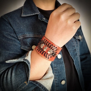 Detail of men's punk wide leather bracelet with silver skull charms and braided rope cords