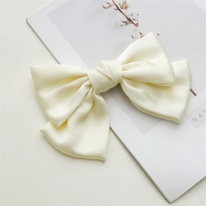 Close-up of a beige satin bow hair clip on a minimalist magazine background