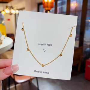 Elegant gold chain necklace featuring five small heart pendants on a white display card