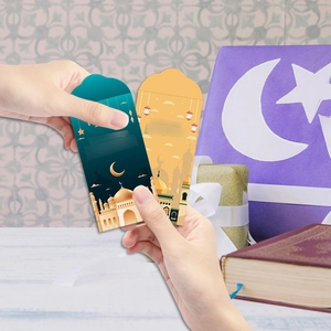 Close-up of hands holding green and yellow Eid Mubarak money envelopes with mosque motifs