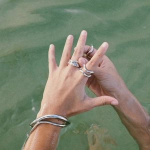 Close-up of liquid-style silver stainless steel rings on hands in clear green water