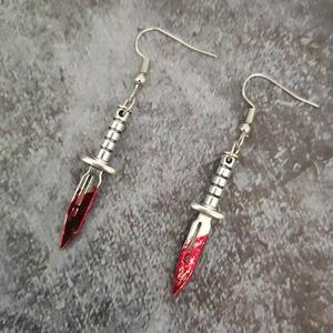 Gothic silver dagger drop earrings with red blood stains on dark stone surface