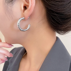 Detailed view of silver C-shaped hoop earrings with bamboo texture on a model