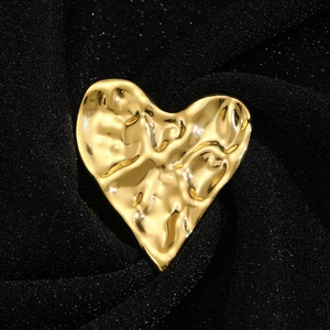 Vue macro d'une broche cœur doré martelé irrégulier sur un tissu plissé noir