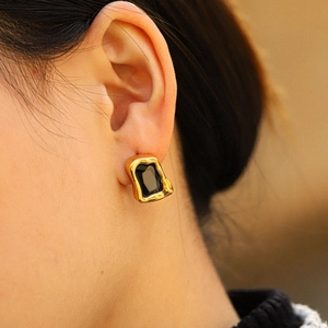 Close-up of gold stainless steel earrings with black square gemstone on model's ear